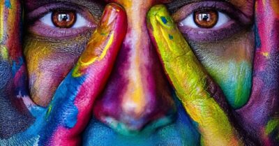 Close-up of a person's face with colorful paint, emphasizing emotional complexity.