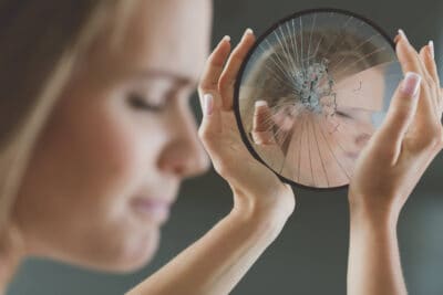 Woman holding a shattered mirror symbolizing self-esteem issues and mental health challenges.